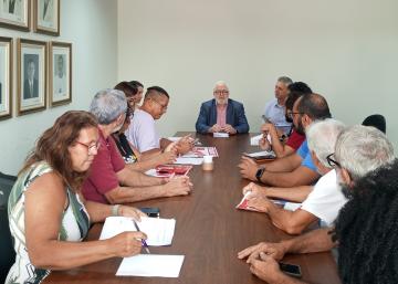 Pessoas presentes na reunião, sentadas em volta de uma mesa de madeira, com o reitor da Ufes sentado na cabeceira