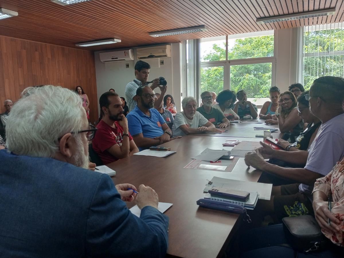 Reitor da Ufes recebe representantes do Sintufes Pessoas presentes na reunião, sentadas em volta de uma mesa de madeira
