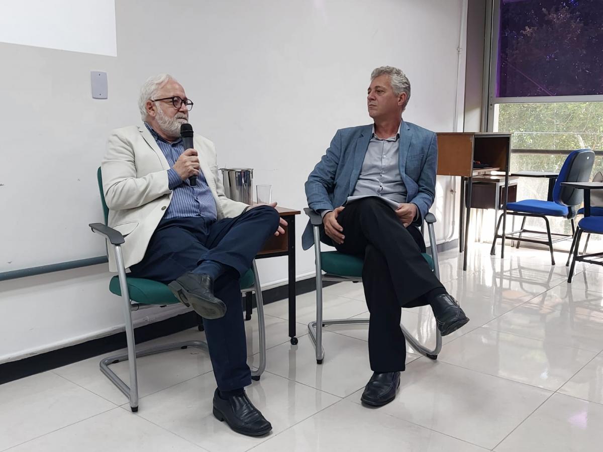 Reitor e vice-reitor da Ufes Reitor e vice-reitor da Ufes sentados em cadeiras, com o reitor falando ao microfone e o vice-reitor olhando para ele