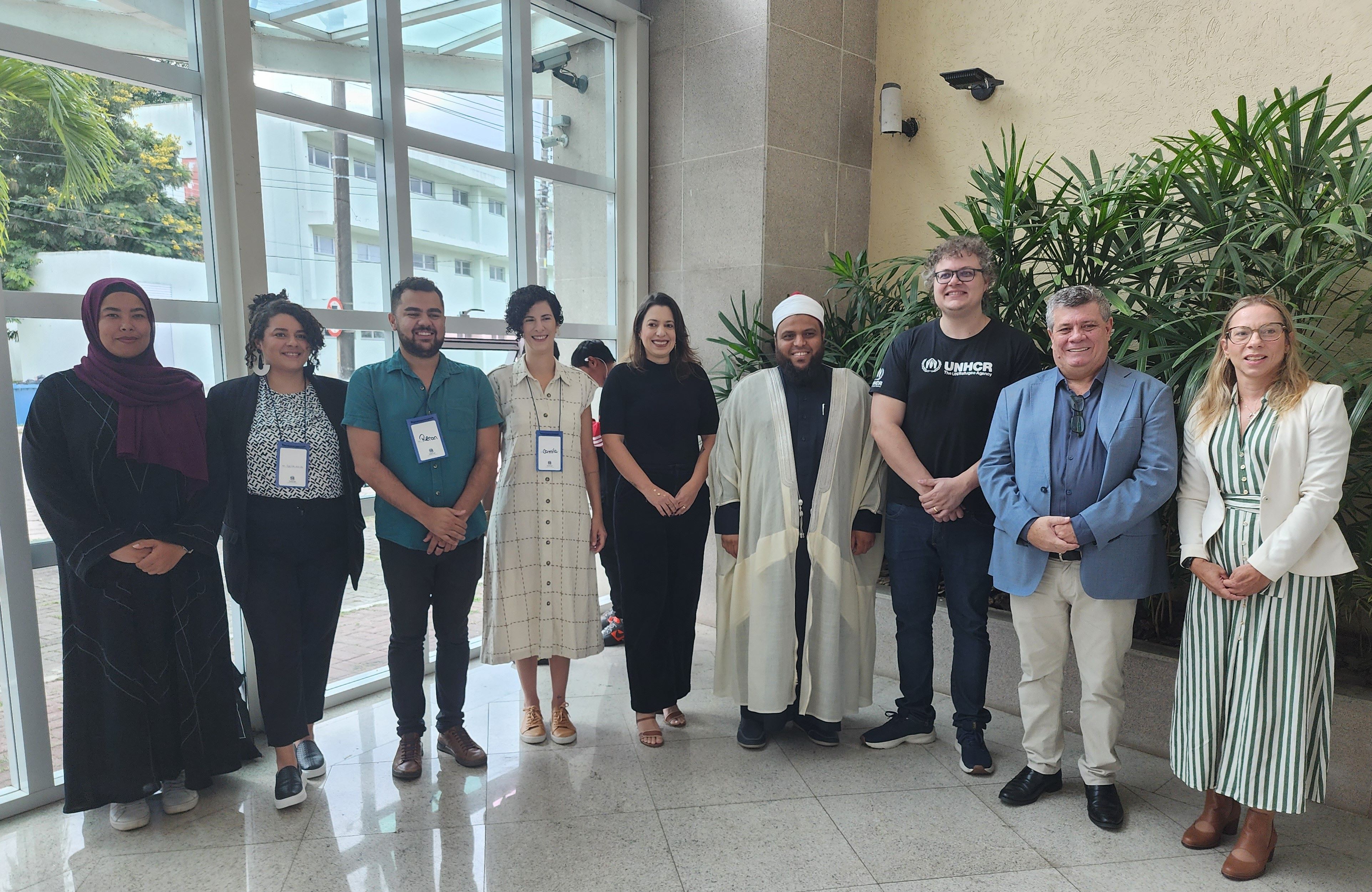 Representantes de povos migrantes, da ONU e da Ufes posam no hall de entrada do Labpetro. 