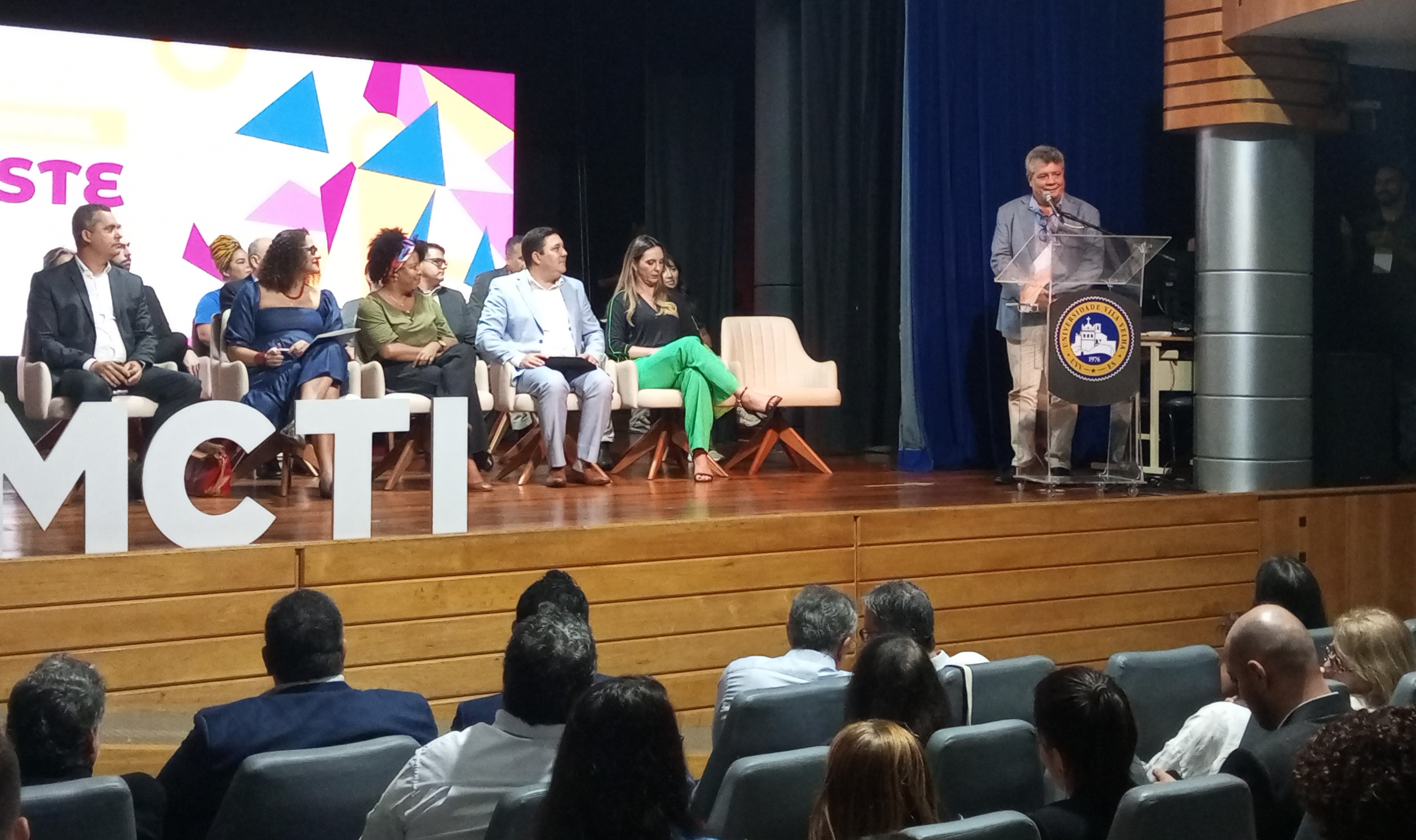 O reitor Eustáquio de Castro na abertura da Etapa Sudeste da Conferência Na foto, o reitor, em pé, fala para a plateia na abertura do evento. Junto com ele no palco estão outras autoridades participantes.