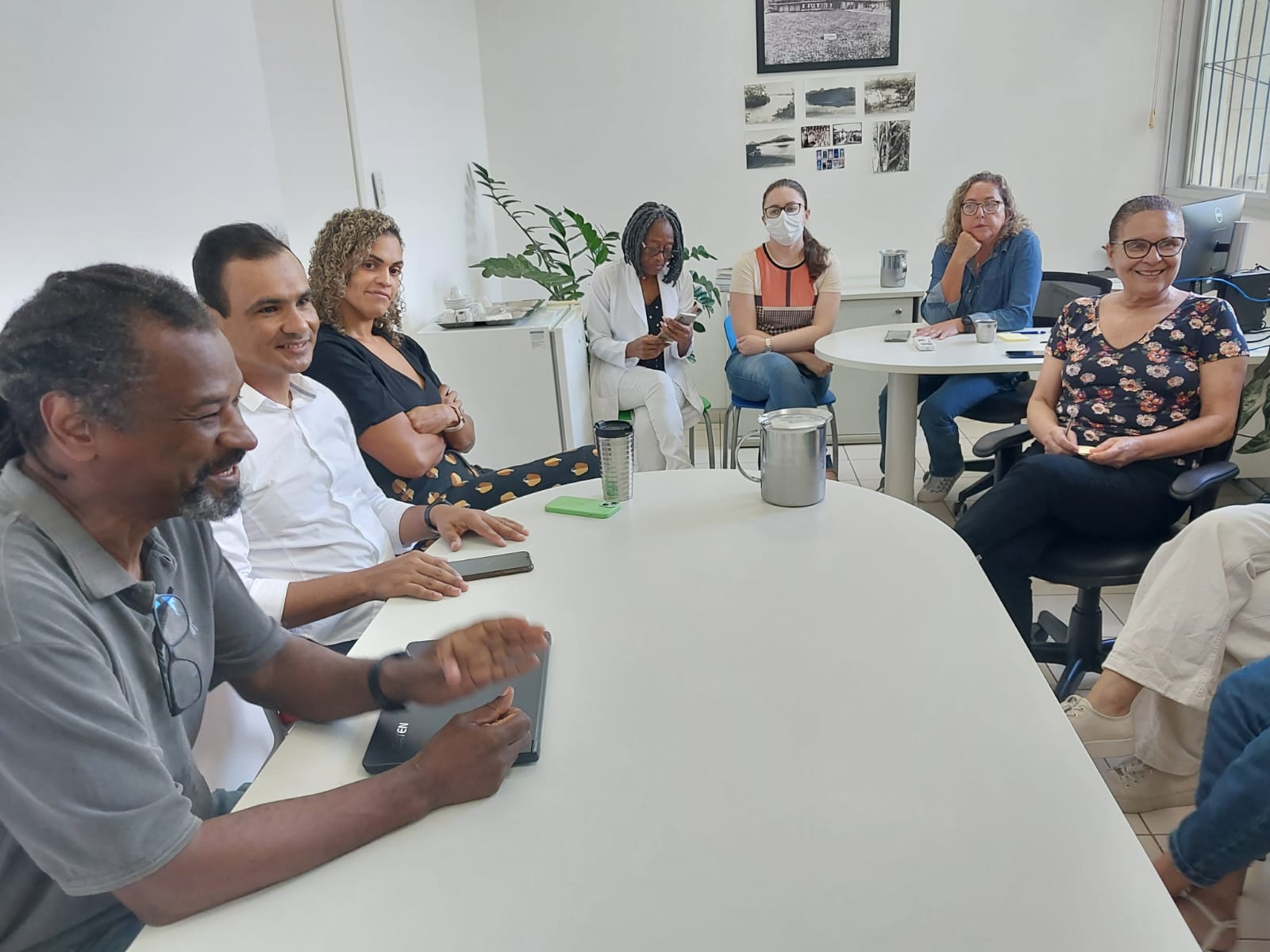 O pró-reitor Antônio Carlos Moraes (de camisa cinza) e do diretor Iury Pessôa (de camisa branca) com a equipe do RU Foto do pró-reitor Antônio Carlos Moraes e do diretor Iury Pessôa sentados à mesa diante da equipe do RU.