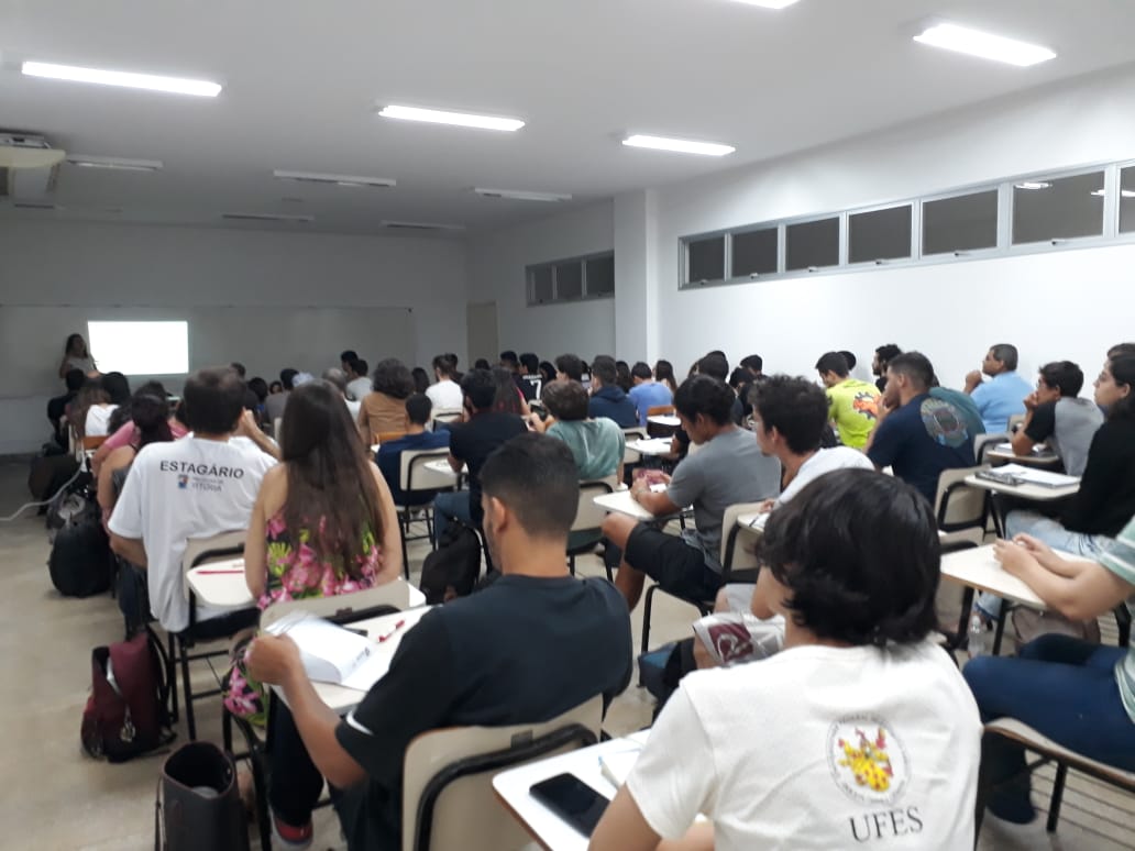 Sala de aula cheia com estudantes e professor ao fundo