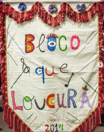 Bandeira com o nome "Bloco que loucura", escrito com letras coloridas num fundo bege