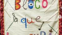 Bandeira com o nome "Bloco que loucura", escrito com letras coloridas num fundo bege