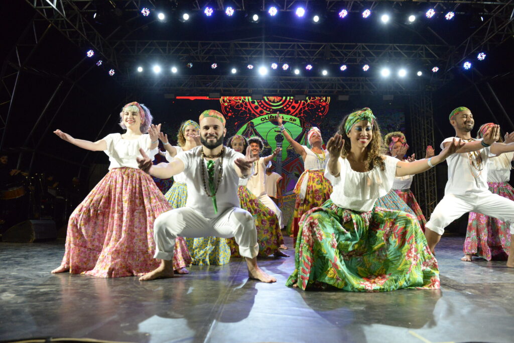 Na foto, integrantes do grupo Andora estão agachados e com mãos estendidas durante dança