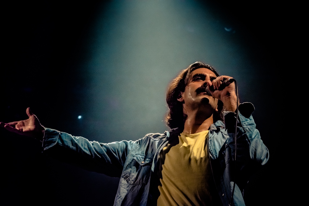 Foto do ator Pablo Paleólogo cantando caracterizado como Belchior