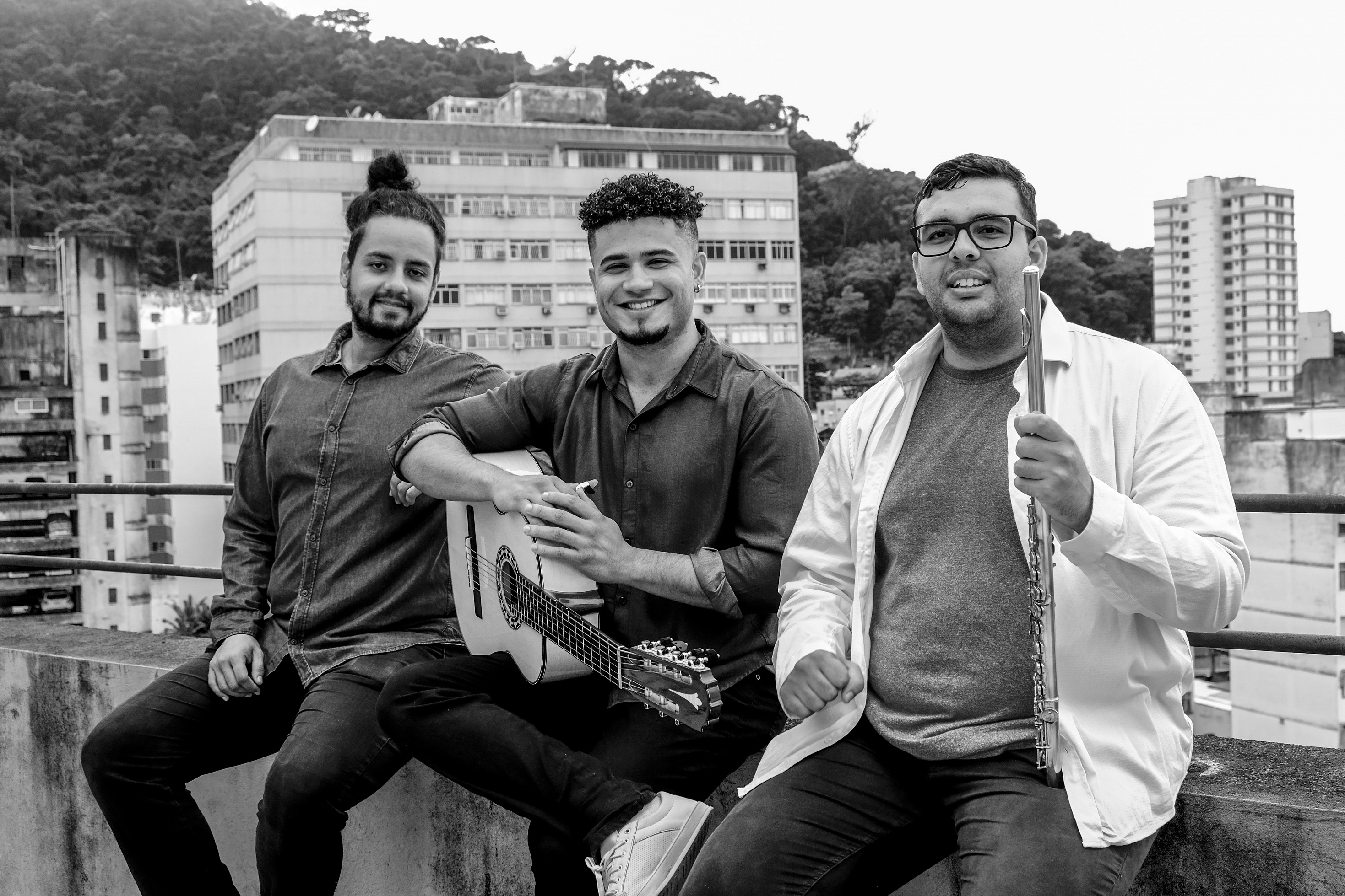 Léo de Paula, Luciano Furtado e Matheus Viana Foto em preto e branco de Léo de Paula, Luciano Furtado e Matheus Viana sentados na mureta de um viaduto, com prédios ao fundo.