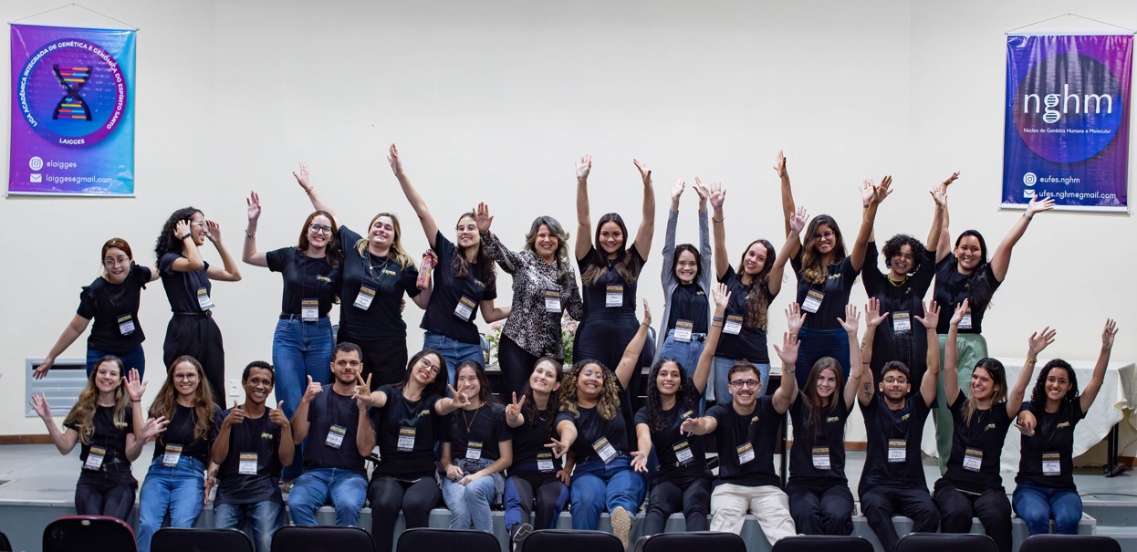 Integrantes da Liga de Genética e Genômica do ES Foto dos integrantes da liga reunidos, todos vestindo camisas pretas e com os braços para cima, em comemoração