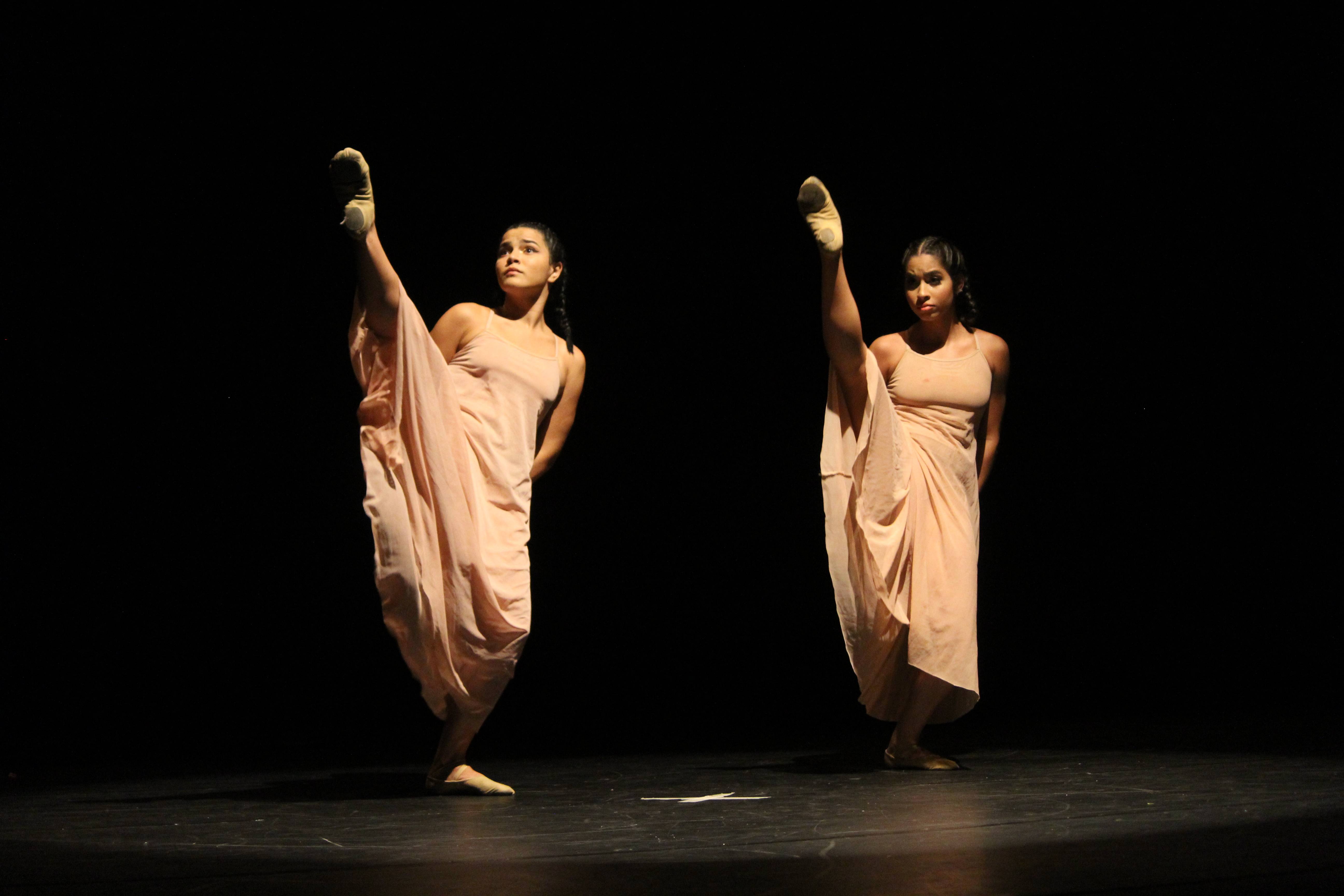 Duas bailarinas com vestidos claros fazem coreografia em um palco.