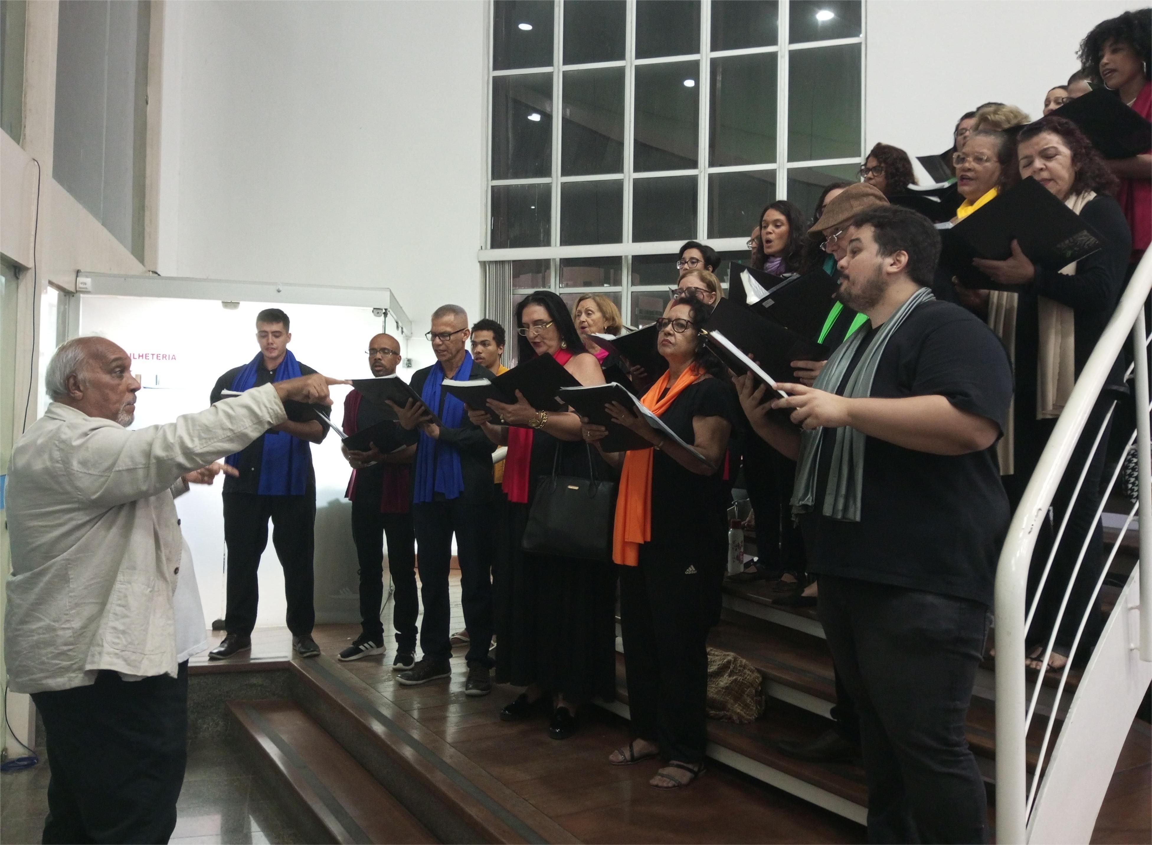 Foto do coral da Ufes, na escada do hall de entrada do Teatro Universitário, recebendo o público
