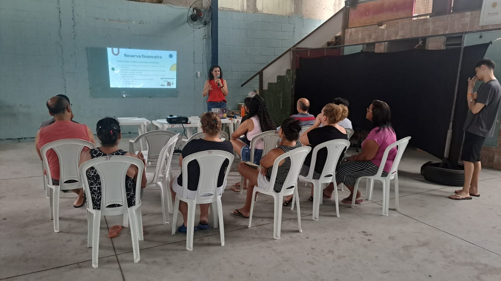 Palestras em comunidades Grupo de pessoas sentadas ouvido uma palestra em um salão.