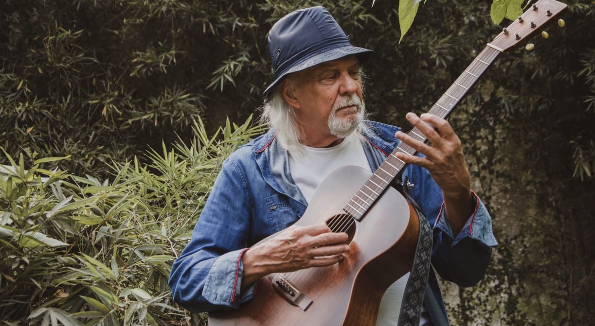 Zé Geraldo Foto do cantor Zé Geraldo tocando violão em uma área verde.