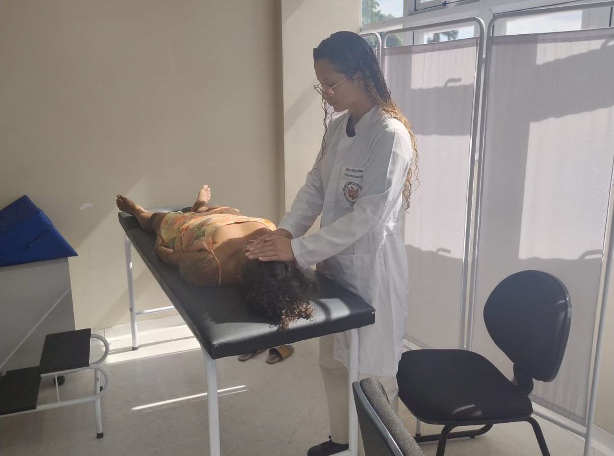 Aplicação de reiki Profissional da Ufes aplica reiki em uma paciente deitada em uma maca.
