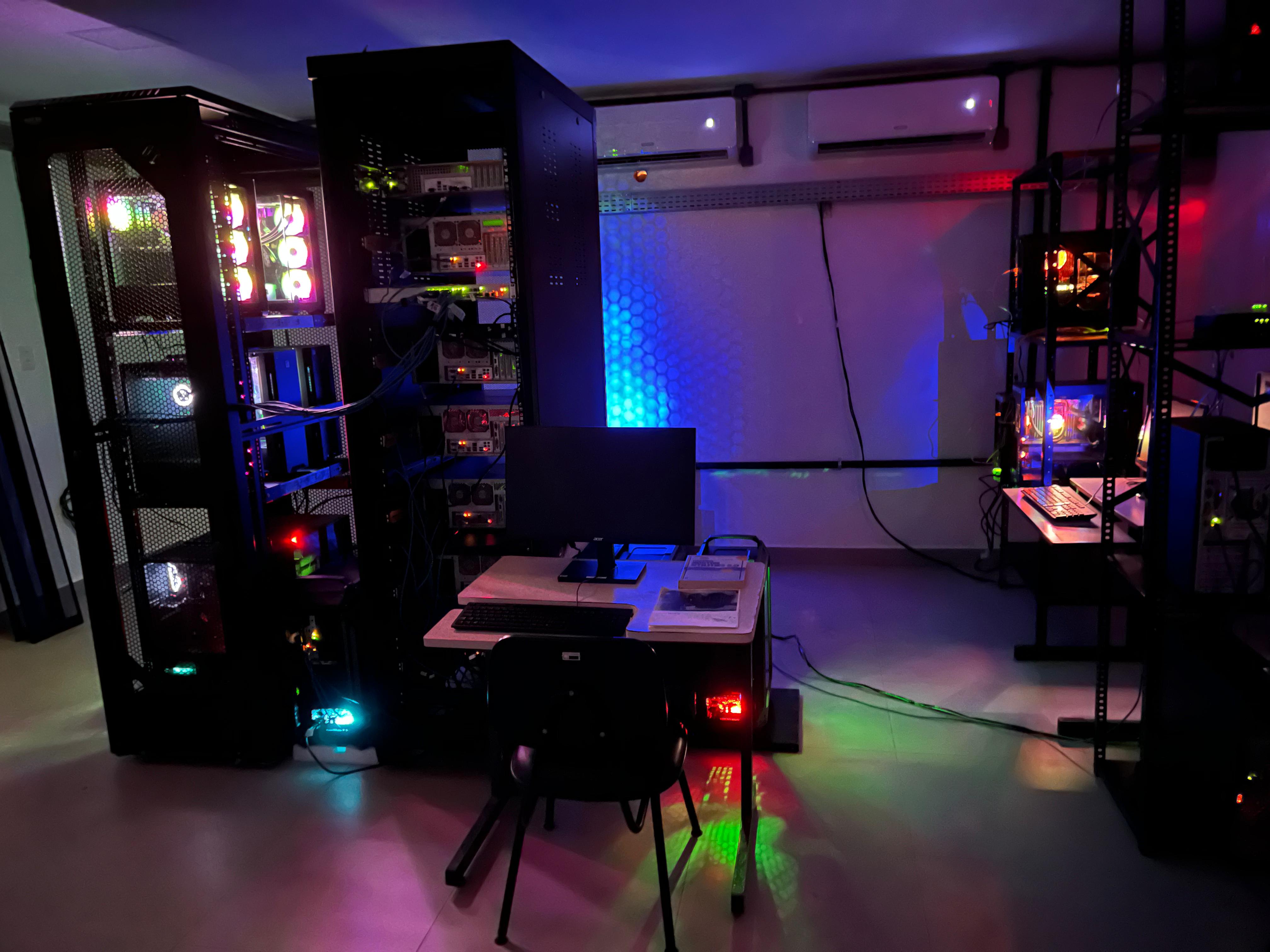 Laboratório Multiusuário de Computação Científica Foto do Laboratório Multiusuário de Computação Científica, onde aparecem estantes com computadores em um ambiente escuro com luzes coloridas