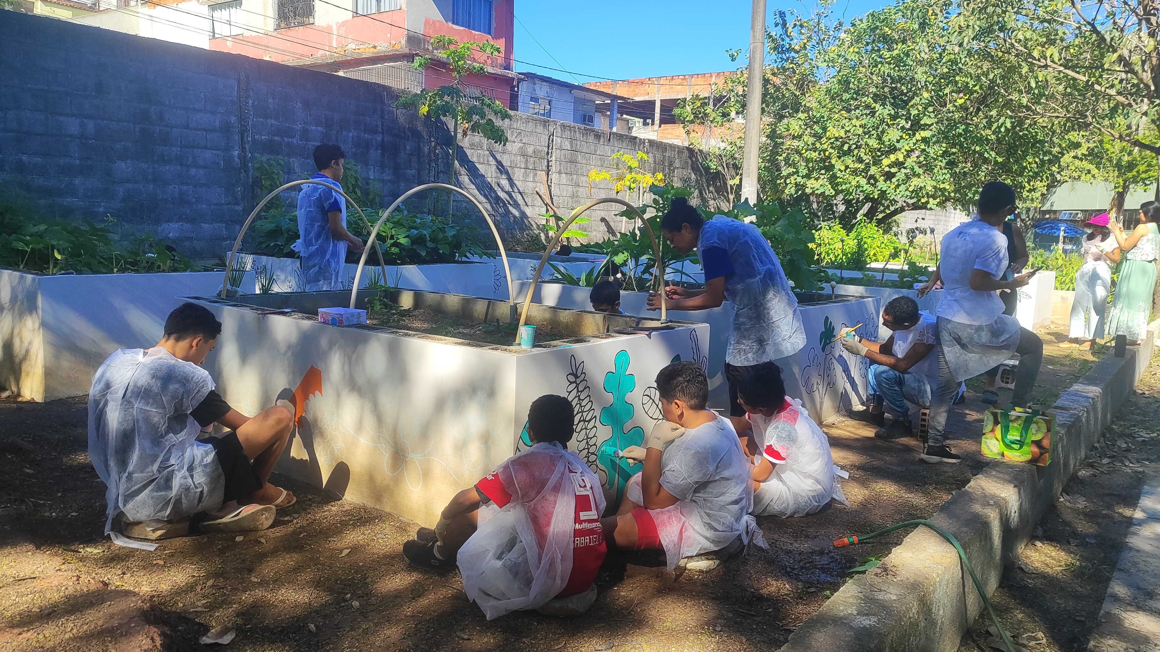 Foto de crianças e monitores pintando as paredes dos canteiros.