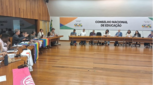Reunião no Conselho Nacional de Educação. Foto da reunião com a presença dos membros do grupo de trabalho em uma grande sala. Ao fundo, uma faixa onde está escrito Conselho Nacional de Educação.