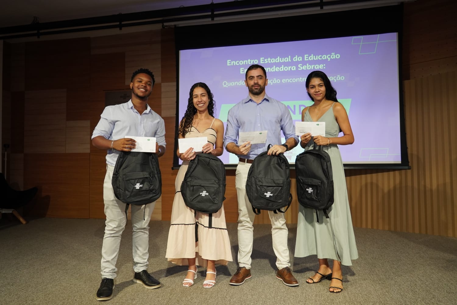 Os estudantes premiados e o professor Gustavo Simão Foto dos estudantes premiados com o professor Gustavo Simão diante do painel de apresentação