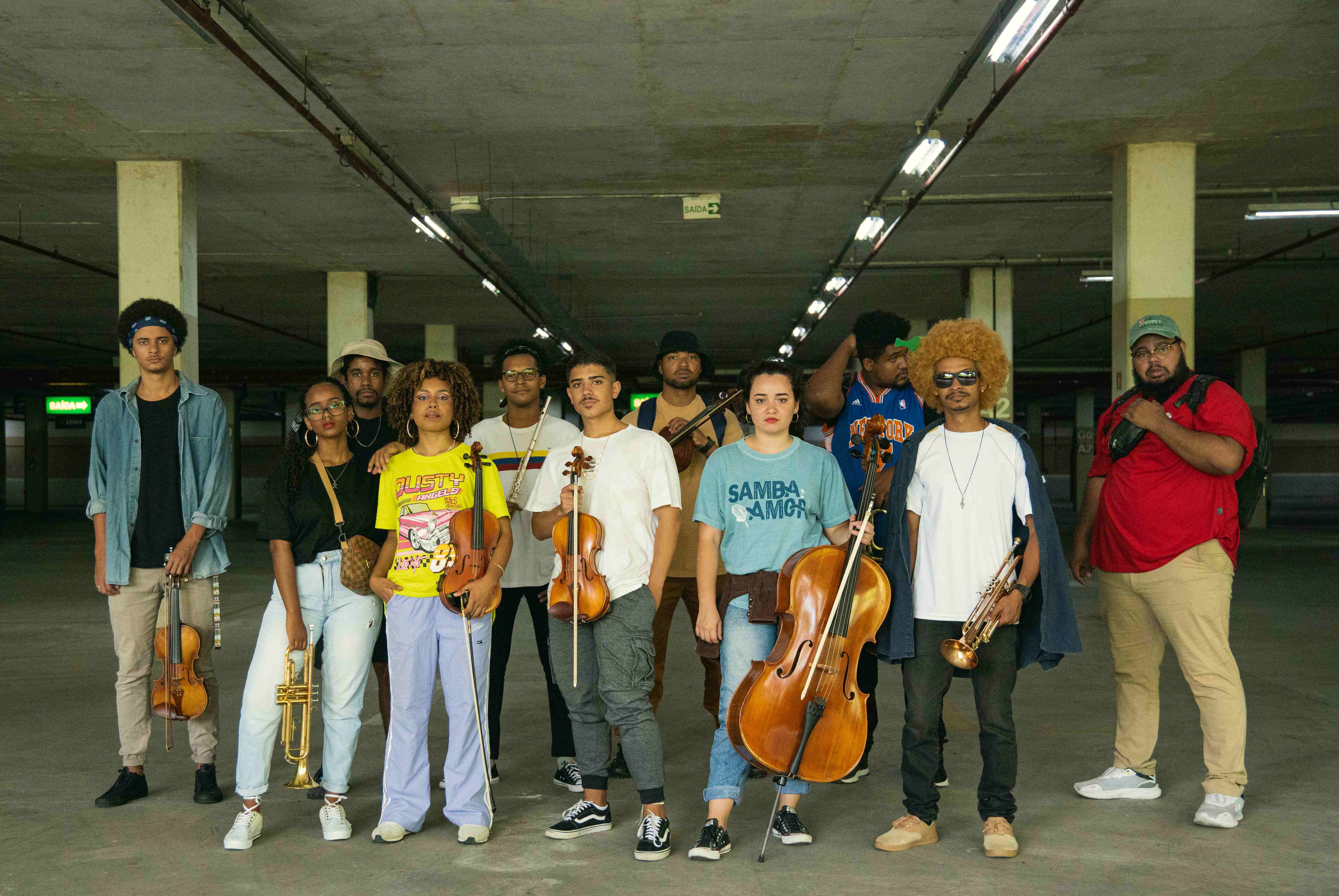 Foto dos integrantes da orquestra vestindo roupas coloridas e posando para a foto em uma garagem