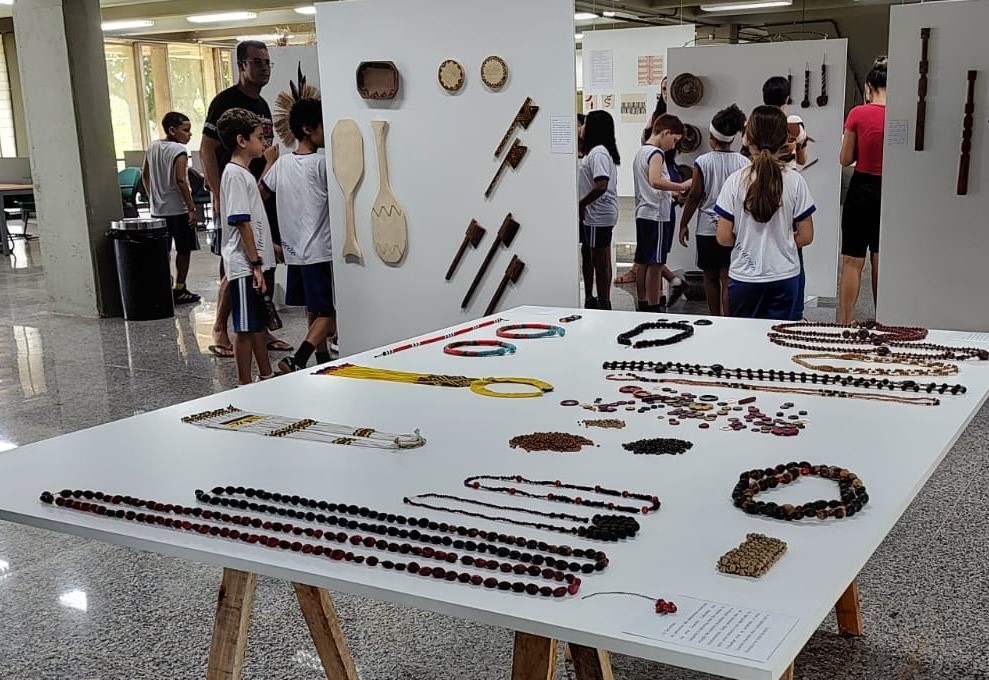 Foto de uma mesa com peças da exposição e os alunos ao fundo