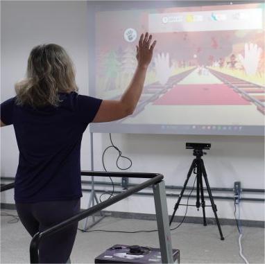 Foto de mulher branca, de costas e com os braços parcialmente levantados, usando roupas pretas e caminhando em uma esteira, de frete para um projetor