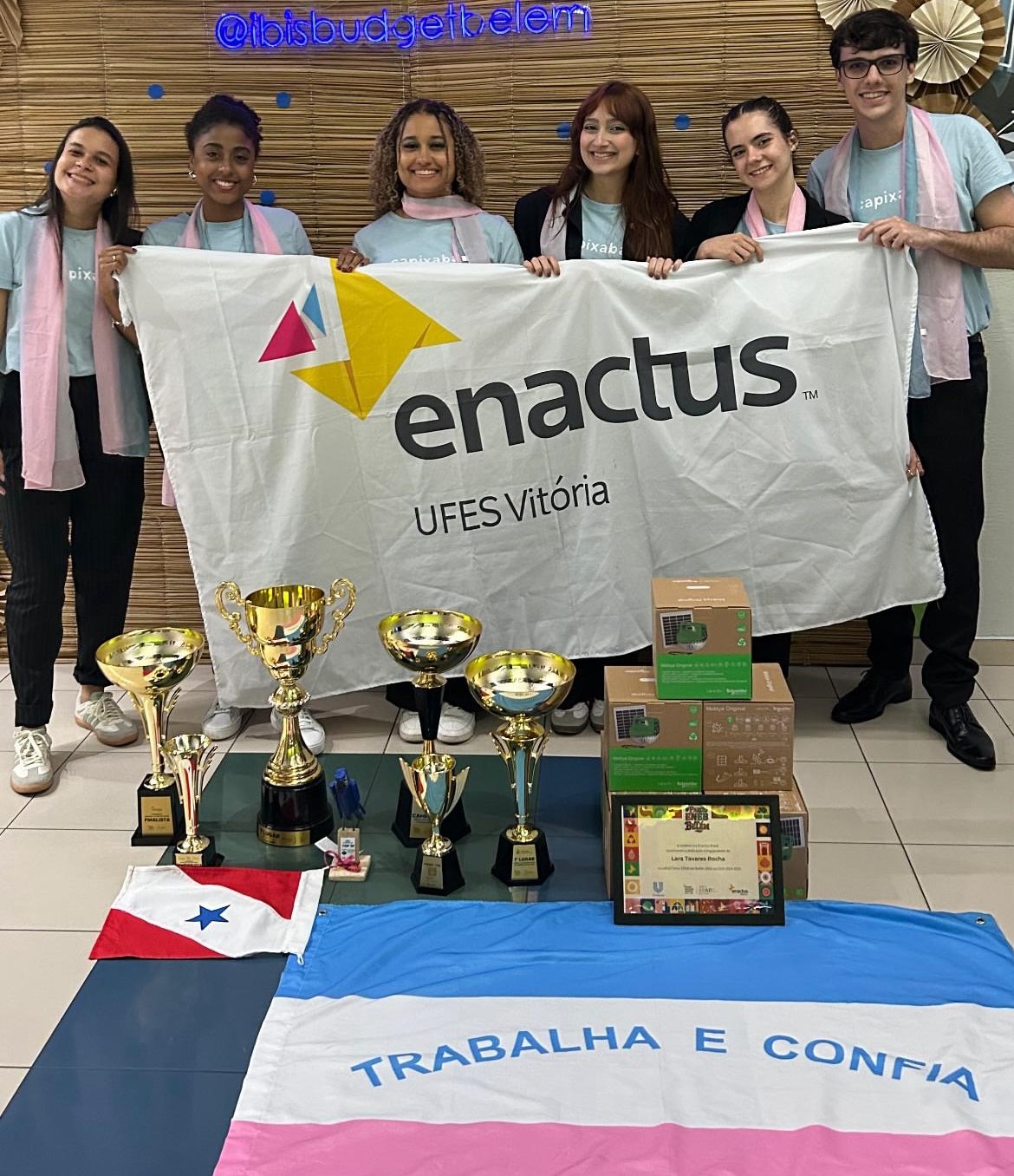 Estudantes exibem a bandeira da Enactus Ufes e os troféus