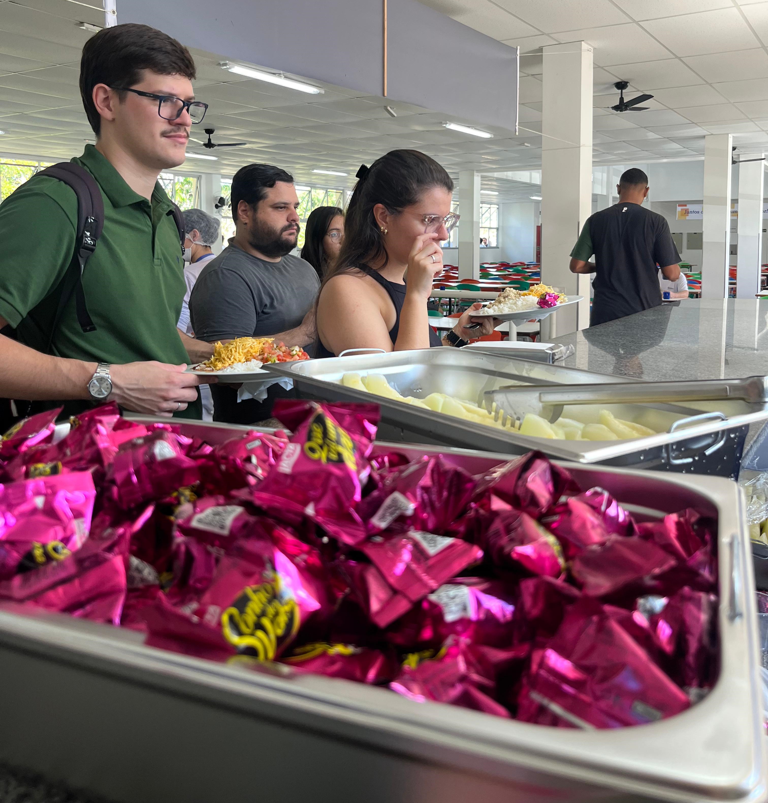 Foto de estudantes se servindo de sobremesa no restaurante, com foco em uma bandeja de bombons