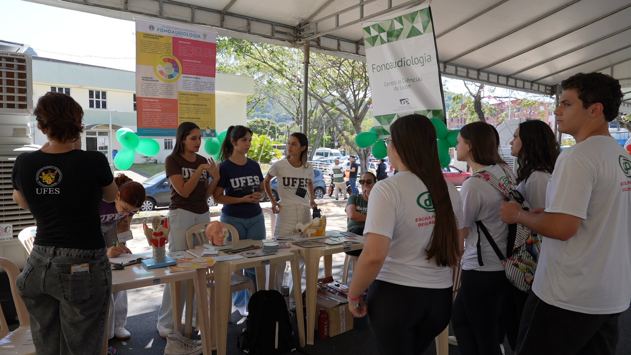 Foto de estudantes ouvindo informações em um estande do curso de Fonoaudiologia