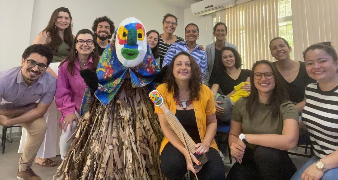 Foto do personagem posando com o grupo de participantes do curso