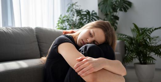 Foto de uma jovem triste, sentada no chão da sala de casa