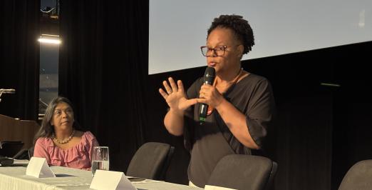 Foto de Joana Guimarães falando. Ao lado, a vice-reitora da Ufes ouvindo