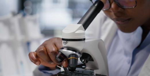 Imagem de uma cientista negra olhando no microscópio_Magnific
