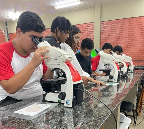 Foto de estudantes em uma sala, olhando em microscópios