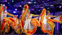 Grupo de dança Flor de Atalaia, do Mato Grosso do Sul. A foto mostra quatro moças em um palco, dançando com vestidos brancos de saia rodada com detalhes em amarelo e vermelho.