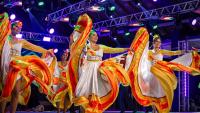 Grupo de dança Flor de Atalaia, do Mato Grosso do Sul. A foto mostra quatro moças em um palco, dançando com vestidos brancos de saia rodada com detalhes em amarelo e vermelho.