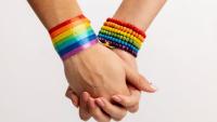 Imagem de duas mãos dadas usando pulseiras nas cores do arco-íris