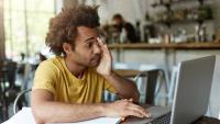 Jovem estudando diante de um notebook com a mão no rosto