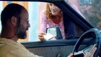 Cena do filme Mambembe, na qual aparece o protagonista dentro de um carro, sendo abordado por uma mulher na janela 