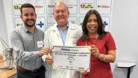Foto do gerente administrativo do Hucam, César Dias, do superintendente do Hospital e da vice-reitora segurando um "voucher tomógrafo"