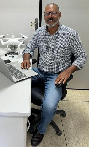 Foto do professor Edney Vitória em frente a um notebook, com um drone sobre a mesa