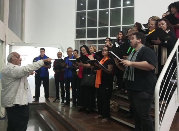 Foto do coral da Ufes, na escada do hall de entrada do Teatro Universitário, recebendo o público