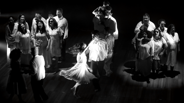 Foto dos cantores em volta de um casal que dança no centro do palco, com a moça rodopiando