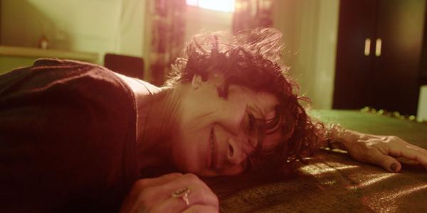 Cena de Lispectorante, onde a personagem aparece deitada de bruços sobre uma cama, sorrindo