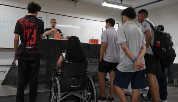 Foto de um grupo de estudantes vendo a apresentação de um experimento