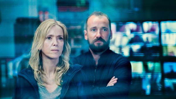 Cena de Caso 137 na qual aparece uma mulher ao lado de um homem em uma sala com monitores