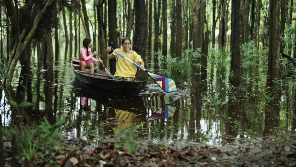 Cena de Sete Cores da Amazônia, na qual aparecem uma menina e uma senhora andando de canoa