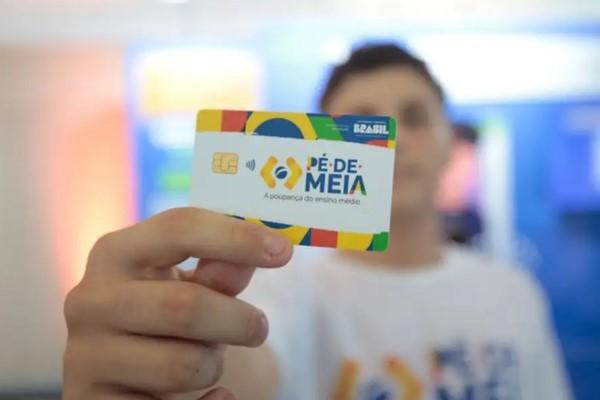 Imagem de um estudante segurando um cartão do programa Pé-de-Meia