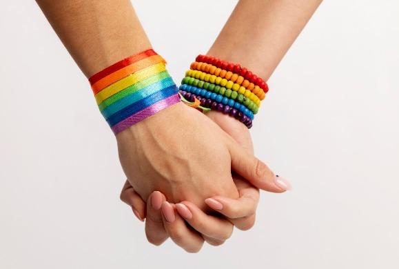 Imagem de duas mãos dadas usando pulseiras nas cores do arco-íris