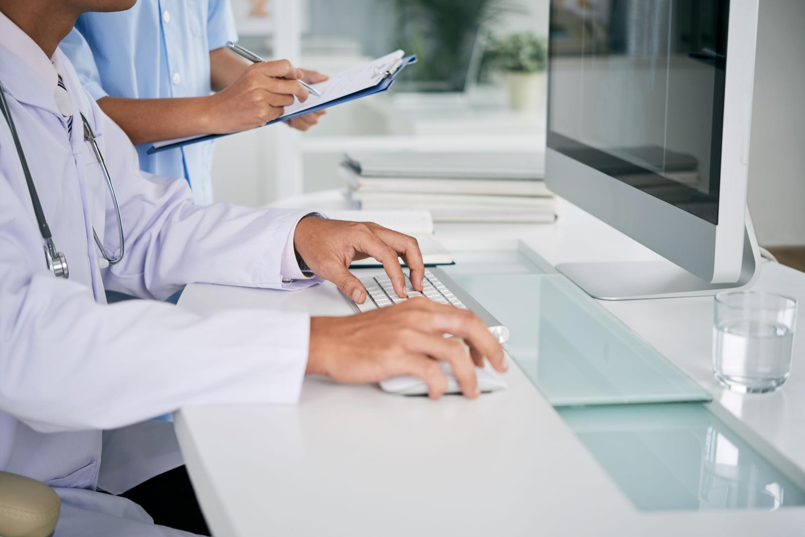 Imagem das mãos de um médico digitando no teclado de um computador