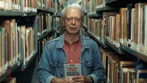 Foto do Frei Betto em uma biblioteca, segurando um livro